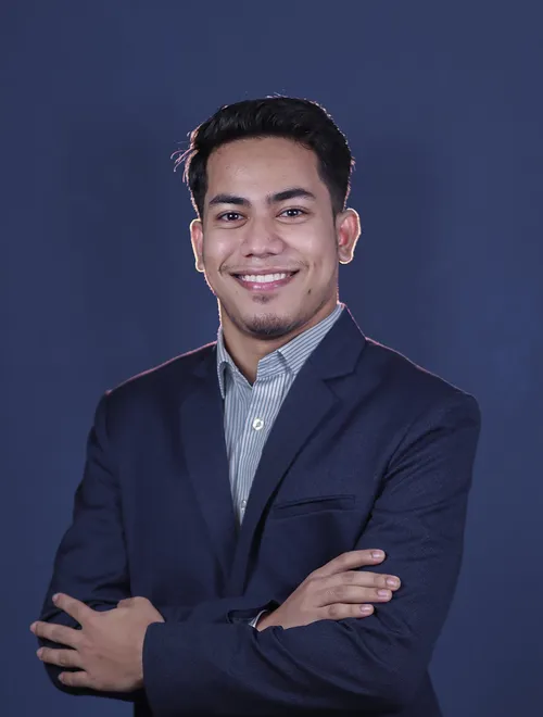 Portrait of Miraj in a navy suit, smiling with arms crossed